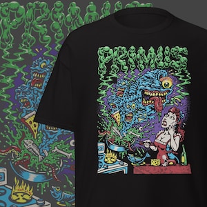 Könnte beinhalten: Schwarzes T-Shirt mit einem farbenfrohen Grafikdesign. Das Design zeigt den Bandnamen "PRIMUS" in Grün, eine surreale Illustration eines Monsters, einer kochenden Frau und andere bizarre Elemente. Der Stil erinnert an einen Comic.