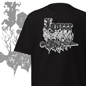 May include: Black t-shirt with a white graphic design. The design features stylized text and abstract shapes. The shirt has a crew neck and short sleeves. A grey silhouette of a tree is on the left side.