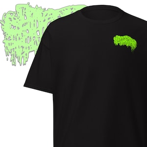 May include: Black t-shirt with a neon green graphic on the chest and a larger, similar design in the background. The graphic appears to be a stylized, dripping shape. The shirt is made of a soft material.