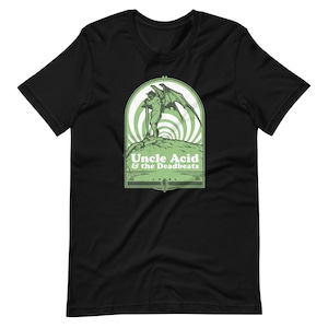 May include: Black t-shirt featuring a green graphic of a winged figure holding a sword, set within a green and white arched design. The text "Uncle Acid & the Deadbeats" is below the graphic. The shirt is made of a soft material.
