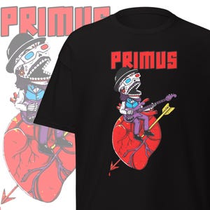 May include: Black t-shirt featuring the word "PRIMUS" in red block letters. The shirt displays a cartoon illustration of a skeleton playing a purple bass guitar while seated on a red heart pierced by a yellow arrow.