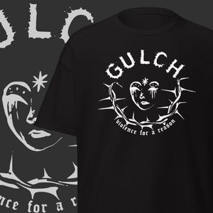 Puede incluir: Camiseta negra con un diseño gráfico blanco de una cara dentro de una corona de espinas, con el nombre de la banda "GULCH" arriba y la frase "violence for a reason" abajo. Un diseño similar está a la izquierda.