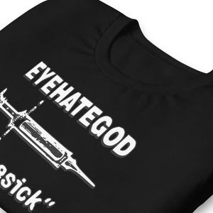 Op de afbeelding: Zwart T-shirt met de witte tekst "EYEHATEGOD" en een spuit-afbeelding. Het shirt heeft ook het woord "sick" in het wit. Het ontwerp is gedrukt op een zwart T-shirt met korte mouwen.