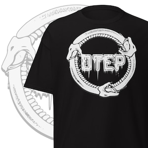Puede incluir: Camiseta negra con un diseño gráfico blanco. El diseño incluye la palabra "OTEP" en una fuente estilizada dentro de un marco circular con cabezas de serpiente. Un gráfico similar es parcialmente visible a la izquierda.