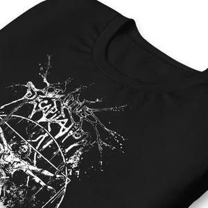 Puede incluir: Camiseta negra con un diseño gráfico blanco. El diseño incluye texto estilizado y una ilustración. La camiseta tiene cuello redondo y mangas cortas. El gráfico parece ser el logotipo de una banda o la portada de un álbum.