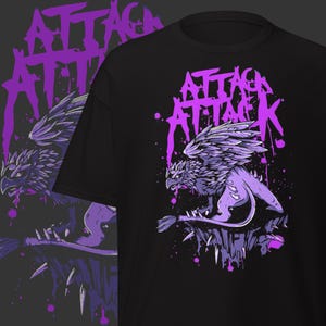 May include: Black t-shirt with a purple griffin illustration and the words "ATTACK ATTACK". The design includes a winged creature on a rocky outcrop, with purple paint splatter effects.