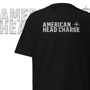 May include: Black t-shirt with the text "AMERICAN HEAD CHARGE" in distressed white lettering. A target graphic is to the right of the text. The shirt is a basic crew neck style.