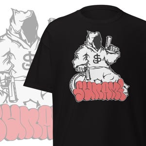 May include: Black t-shirt featuring a white and red graphic. The graphic depicts a hooded figure holding two objects, with a dollar sign on the chest. The word "SHURAKZ" is written in red graffiti style.