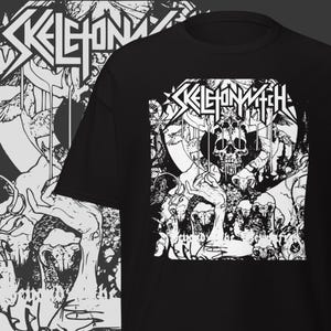 May include: Black t-shirt featuring a white graphic design. The design includes the band name "SKELETONWITCH" in a stylized font above a detailed illustration of a skull and other macabre elements. The shirt has a crew neck and short sleeves.