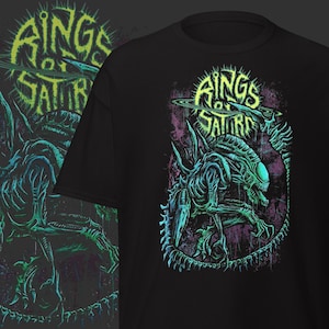 May include: Black t-shirt featuring a detailed illustration of an alien creature with the text "Rings of Saturn" in a neon green font. The alien is depicted in shades of teal and green, set against a purple and black background.