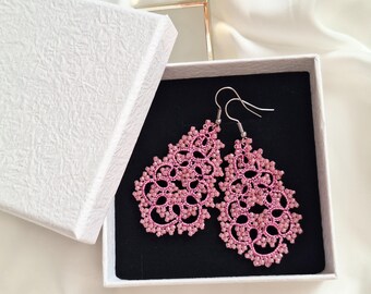 May include: Pink lace earrings with a floral design, presented in an open white gift box with a black interior. The earrings feature a beaded texture and silver hooks. The box has a textured surface.