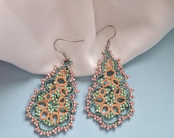 May include: A pair of handmade dangle earrings. The earrings have a detailed, openwork design in teal, peach, and pink. The intricate pattern is accented with small beads, and they hang from silver-coloured hooks.