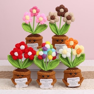 May include: A collection of handmade crochet flowers in brown pots. The flowers are in various colors, including pink, red, white, orange, and multicolored. Each pot has a smiling face and a small sign that reads "Emotional Support Plant."