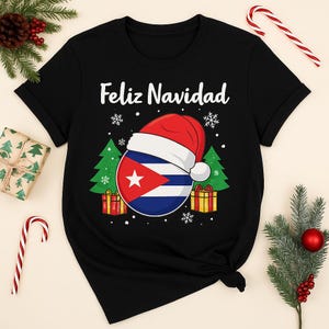 Peut inclure: T-shirt noir avec l'inscription blanche "Feliz Navidad". Le t-shirt présente un graphisme d'ornement de Noël avec le drapeau cubain, un bonnet de Père Noël, des flocons de neige, des sapins et des cadeaux.