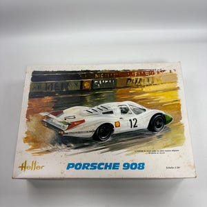 May include: A Heller model kit box for a Porsche 908 race car. The box features an illustration of a white Porsche 908 with the number 12 on the side, driving on a track. The text reads Heller, PORSCHE 908, and Echelle 1/24 on the front.