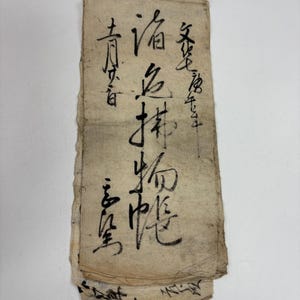 May include: A vintage, rectangular scroll with handwritten black ink calligraphy. The paper is aged, with visible creases and a loop at the top for hanging. The text is in vertical columns, with the characters appearing to be of East Asian origin.