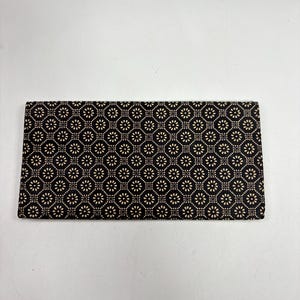 May include: A rectangular clutch bag featuring a black fabric base with a repeating geometric pattern of small, light beige flower-like shapes arranged in a grid. The design consists of interconnected circles and dots across the surface.