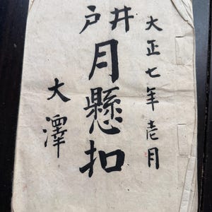 Könnte beinhalten: Ein vergilbtes Papierdokument mit japanischer Kalligraphie in schwarzer Tinte. Der Text ist in vertikalen Spalten angeordnet, einschließlich des Titels "月懸扣". Das Papier weist Alterserscheinungen auf, mit Knicken und Abnutzung.