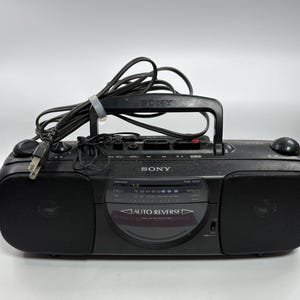 Könnte beinhalten: Ein schwarzer, tragbarer Sony Kassettenrekorder mit Radio, ausgestattet mit einem Tragegriff, integrierten Lautsprechern an beiden Seiten, einem zentralen Sendersuchlauf für FM und AM sowie einem Kassettenfach mit der Aufschrift AUTO REVERSE.