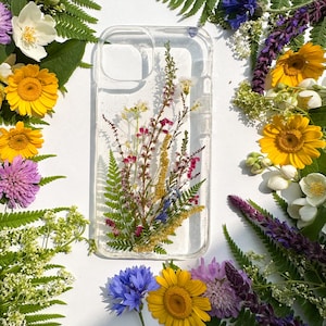 May include: Clear phone case with embedded dried flowers, including yellow daisies, purple lavender, and green ferns. The case is surrounded by a border of fresh flowers on a white background.