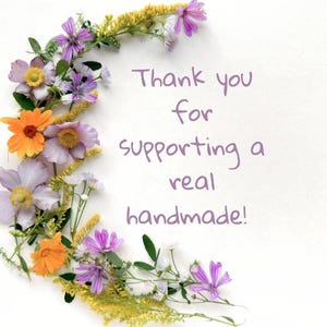 May include: A white background with a floral arrangement of orange, purple, and yellow flowers. The text reads, "Thank you for supporting a real handmade!"