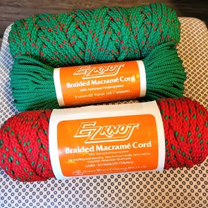 May include: Two spools of EZ Knot Braided Macramé Cord. One is green with red accents, the other is red with green accents. The labels read "100% Texturized Polypropylene" and "50 Yards (45.7 Meters)". The cord is for knotting and weaving.