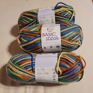 May include: Three balls of Basic Stitch yarn in a vibrant blend of blue, yellow, orange, and green. Each ball is labelled with the weight, 85g, and length, 140m. The yarn is anti-pilling and machine washable.