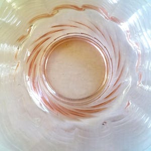 May include: A clear glass bowl with a scalloped rim and a spiral design in the center. The bowl has a light pink hue and a circular base. The glass has a wavy texture.