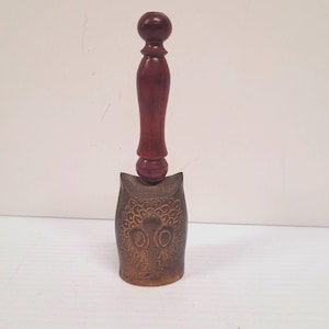 May include: A decorative owl-shaped bell with a dark brown wooden handle. The bell has a detailed owl face design and a dark brown finish. The handle is a deep reddish-brown color.