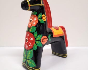 May include: A black wooden Dala horse figurine with red, orange, and white floral designs. The horse has a red mane and tail, and yellow and orange saddle details. The figurine is approximately 6 inches tall.
