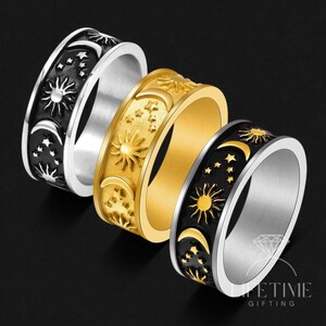 Könnte beinhalten: Drei Ringe mit Himmelsmotiven in Silber, Gold und Schwarz. Jeder Ring zeigt Sonnen, Monde und Sterne. Die Ringe sind aus Metall und haben eine polierte Oberfläche. Die Ringe werden vor einem schwarzen Hintergrund präsentiert.