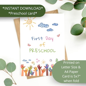 May include: A white card with the text "First Day of Preschool" in colorful lettering, featuring drawings of a sun, clouds, butterflies, and colorful handprints. The card is printed on Letter Size & A4 Paper and is 5x7 inches when folded.