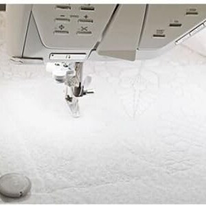 Puede incluir: Una m&aacute;quina de coser blanca con una aguja e hilo en su lugar, lista para coser. La m&aacute;quina est&aacute; sobre una superficie blanca con tres objetos redondos blancos.