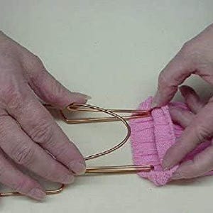 May include: A close-up of a person's hands using a copper wire sock holder to hold a pink sock in place.