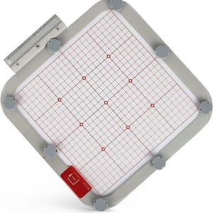 May include: A gray embroidery hoop with a white grid and red dots. The hoop has a silver metal frame and a black label that says "E-P97M ABC".