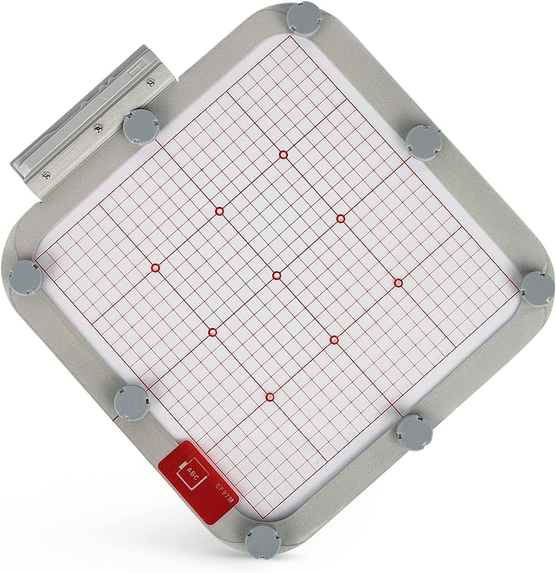 May include: A gray embroidery hoop with a white grid and red dots. The hoop has a silver metal frame and a black label that says "E-P97M ABC".