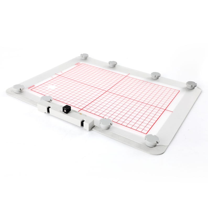 Op de afbeelding: Een witte, rechthoekige borduurring met een rood rasterpatroon en een zwarte schakelaar aan de zijkant. De ring is van metaal en heeft acht zilveren knoppen rondom de omtrek.