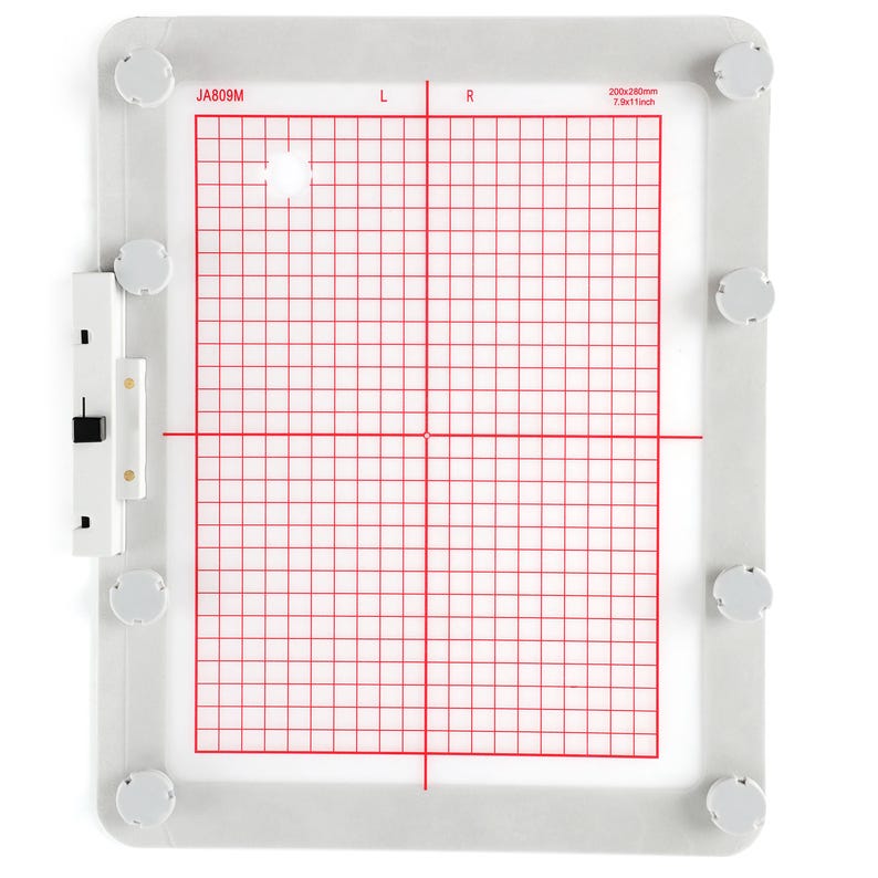 Op de afbeelding: Een witte plastic borduurring met een rood rasterpatroon. De ring is 7,8 x 11 inch en heeft een label met de tekst "JA809M".