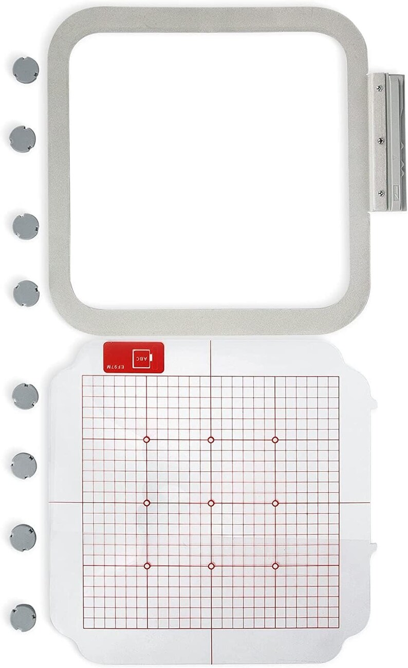 May include: A white embroidery hoop with a clear plastic template inside. The template has a grid pattern with red lines and red dots. The hoop is 5x7 inches and has a silver metal latch.