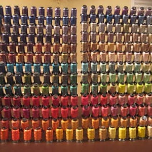 Puede incluir: Una gran colección de coloridas bobinas de hilo, dispuestas en un patrón de cuadrícula. Las bobinas están apiladas, mostrando una amplia gama de colores, desde rojos y naranjas vibrantes hasta azules y verdes fríos. Los hilos parecen ser para coser o manualidades.
