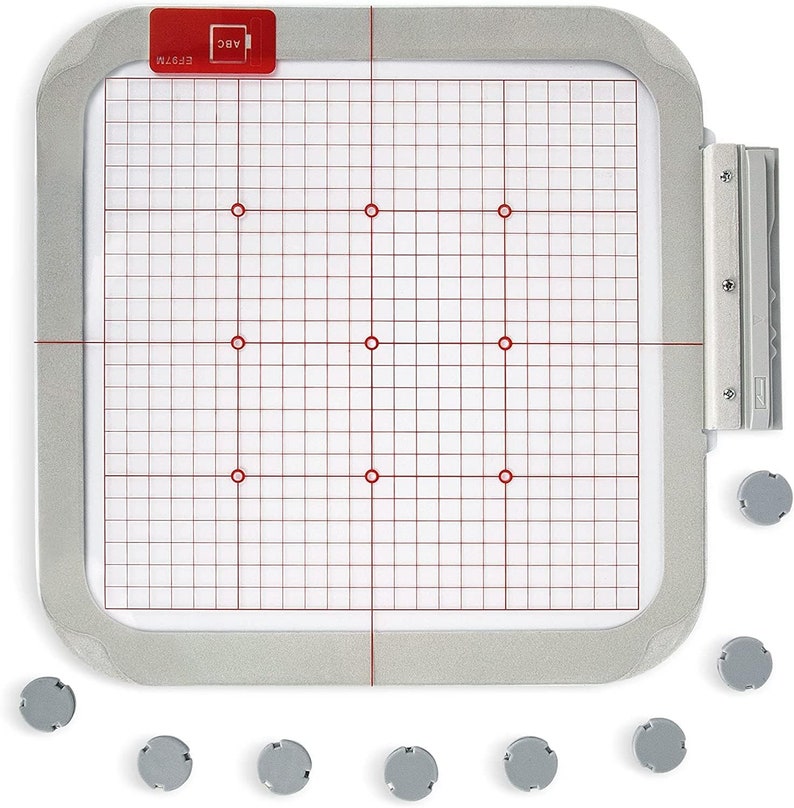 May include: A silver embroidery hoop with a white grid and red markings. The hoop is 10 inches in diameter and has a clear plastic sheet inside. Nine small gray plastic feet are scattered around the hoop.