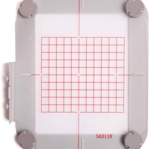 Puede incluir: Un aro de bordado de pl&aacute;stico blanco con un patr&oacute;n de cuadr&iacute;cula roja y el texto "SA311H".