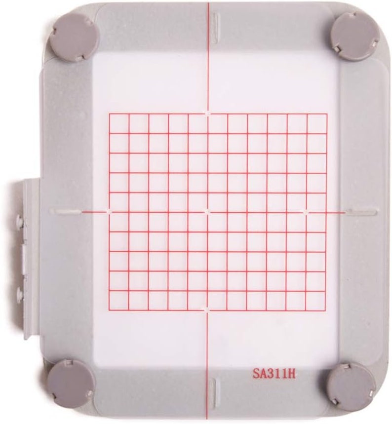 Puede incluir: Un aro de bordado de pl&aacute;stico blanco con un patr&oacute;n de cuadr&iacute;cula roja y el texto "SA311H".