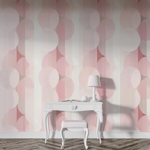Könnte beinhalten: Ein Raum mit einer rosa-weißen Tapete mit überlappenden Kreisen und vertikalen Streifen. Vor der Wand stehen ein weißer Schreibtisch mit passendem Hocker und eine kleine Lampe mit gemustertem Schirm. Ein Buch und eine dekorative Kugel liegen auf dem Schreibtisch.