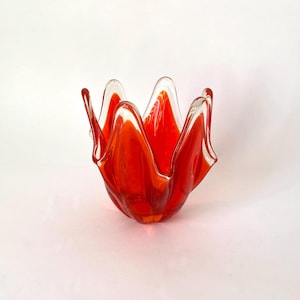 May include: A red glass bowl with a wavy, organic shape. The bowl has a clear glass rim and is perfect for holding small items.