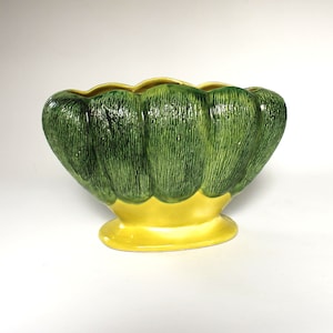 May include: A green and yellow ceramic planter shaped like a flower with five petals. The planter has a textured surface and a yellow base.