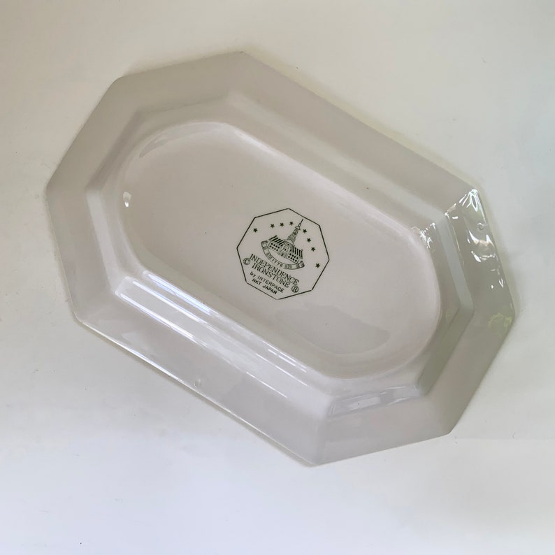 May include: White octagonal serving dish with a green Independence Trading Co. logo featuring a building and stars. The logo also includes the text "The Independence Trading Co. by Stetson, Made in Japan."