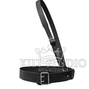 May include: Black leather kilt belt with a matching shoulder strap. The belt has a silver-coloured buckle and adjustment holes. The strap is connected to the belt with a silver-coloured buckle. The text "KILT STUDIO" and "KILT & ACCESSORIES" is visible.
