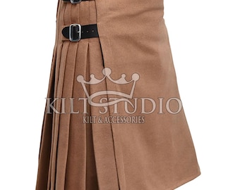 May include: A tan kilt with pleats and two black leather straps with silver buckles. The kilt has the text "KILT STUDIO" and "KILTS & ACCESSORIES" printed on it. The kilt is made of a thick, durable fabric.