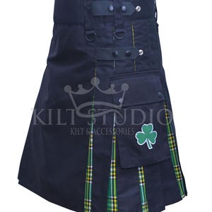 Op de afbeelding: Zwarte kilt met groen en geel geruite details. Voorzien van een zak met een groen klaverblad embleem. De kilt heeft verstelbare bandjes en de tekst "KILT STUDIO KILT & ACCESSORIES".